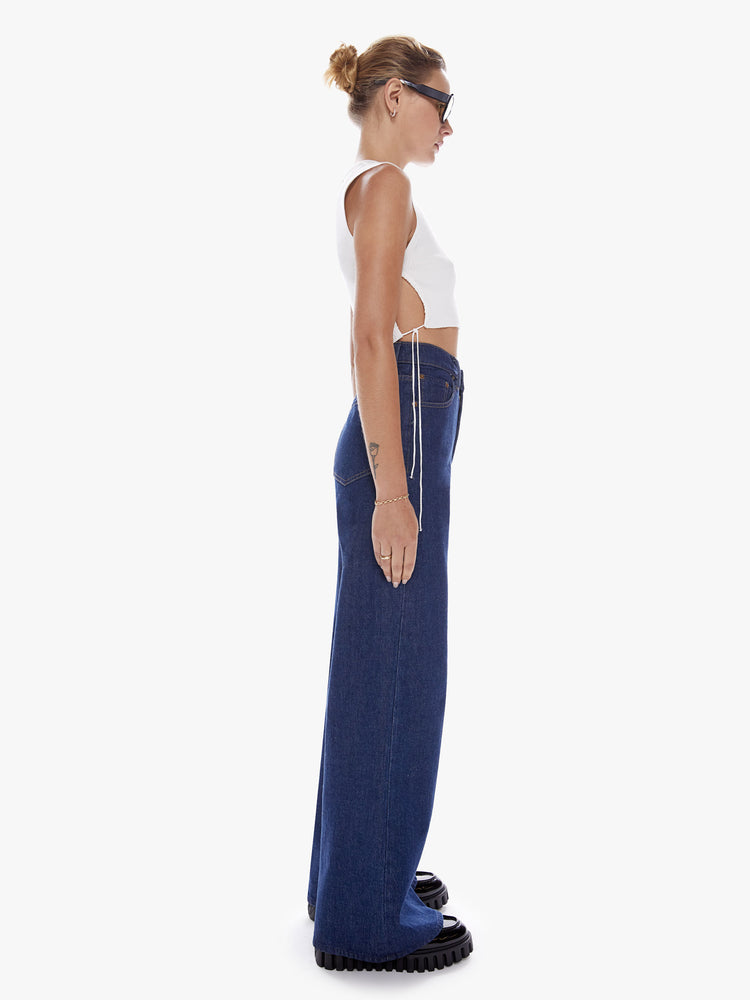 Side full body view of a woman in Snacks widest leg jean from mothers homage to throwback styles of the 80s and 90s, the high rise jeans feature a loose, super full leg and a long 32-inch inseam in a dark blue wash