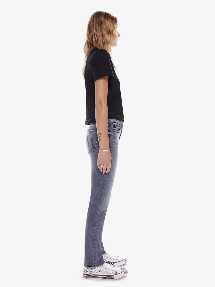 Side full body view of a woman in a midrise straight leg jean with an ankle length inseam and a clean hem in a faded black wash with distressing and tears for a worn-in look