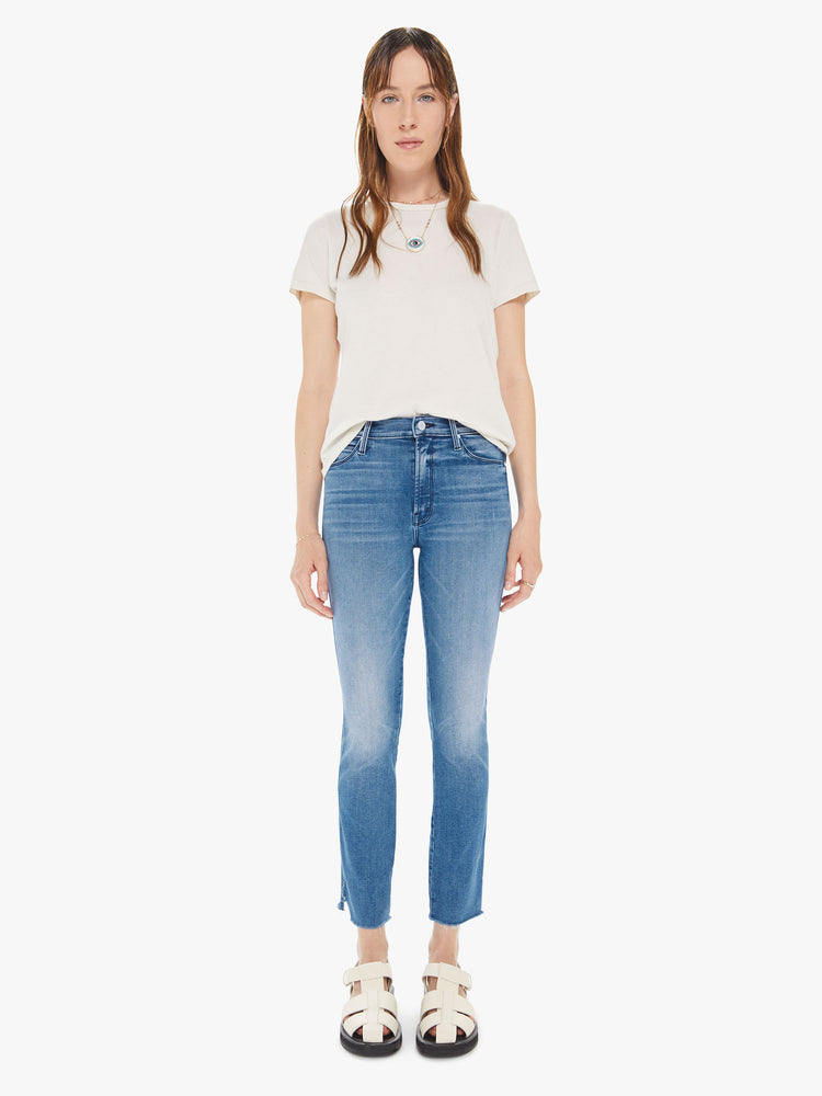 Front view of a womens medium blue wash jean featuring a mid rise, slim straight leg, and a raw cut hem.