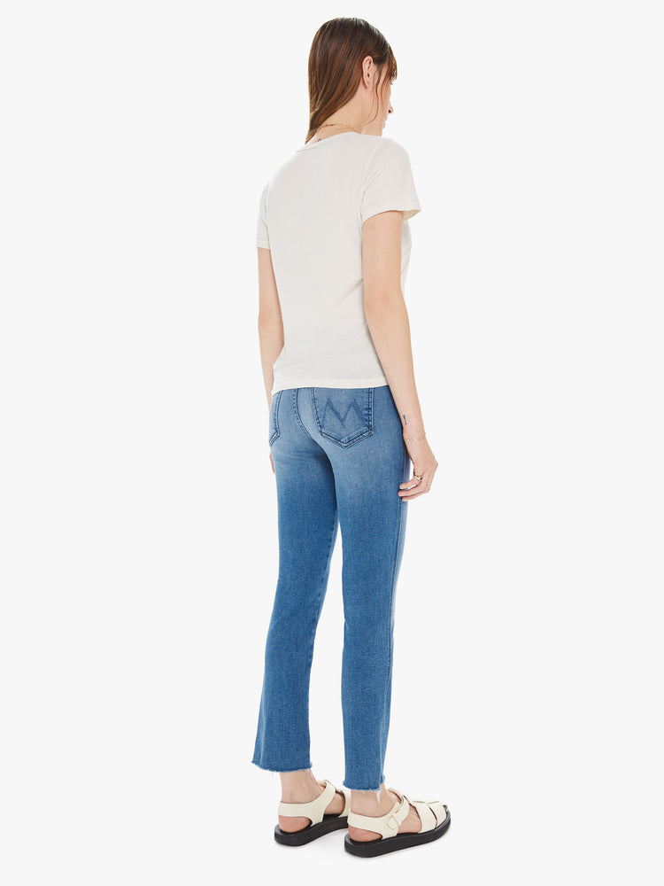 Side view of a womens medium blue wash jean featuring a mid rise, slim straight leg, and a raw cut hem.