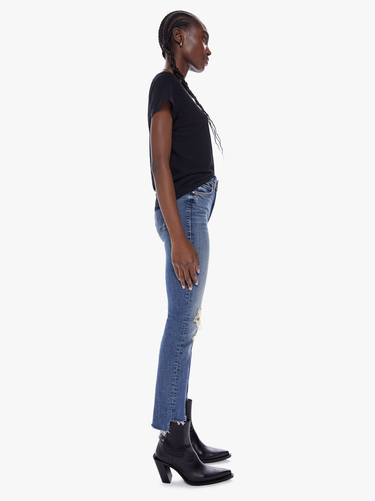 Side view of a womens medium blue wash jean featuring a mid rise, straight leg, distressed details at the knees and an ankle length crop step hem.