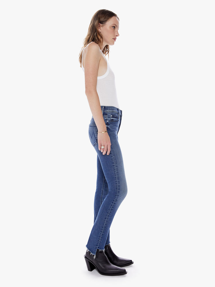 Side view of a woman in our most popular mid rise jean with a straight leg and an ankle length inseam and a frayed step hem made from denim with a touch of stretch in a dark blue wash with subtle fading and whiskering