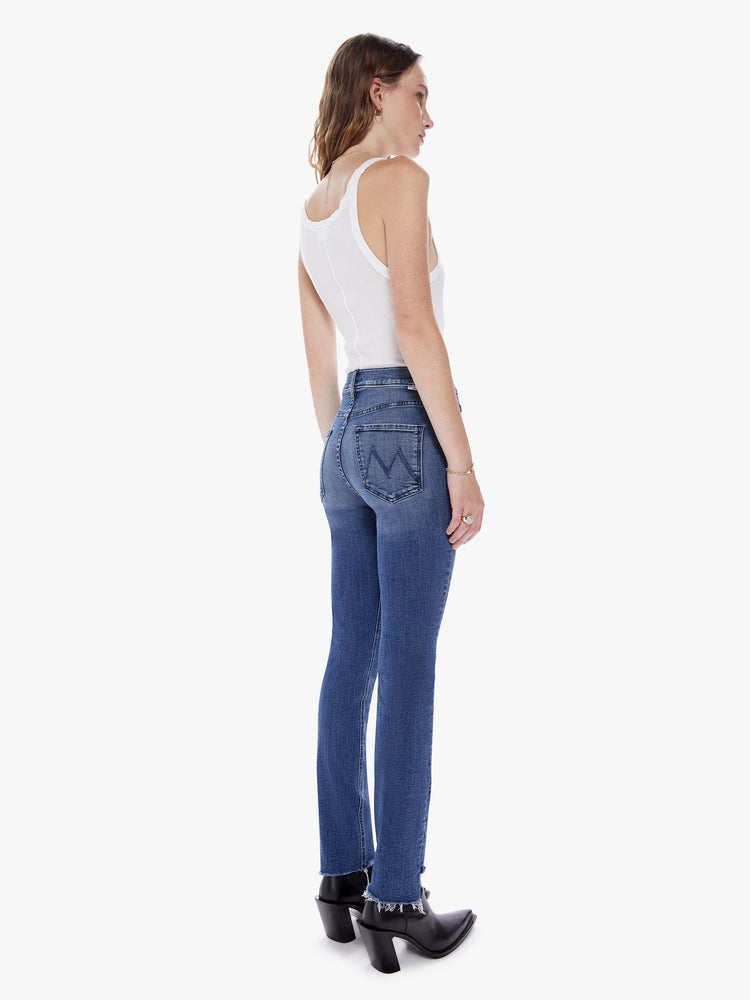 Back view of a woman in our most popular mid rise jean with a straight leg and an ankle length inseam and a frayed step hem made from denim with a touch of stretch in a dark blue wash with subtle fading and whiskering
