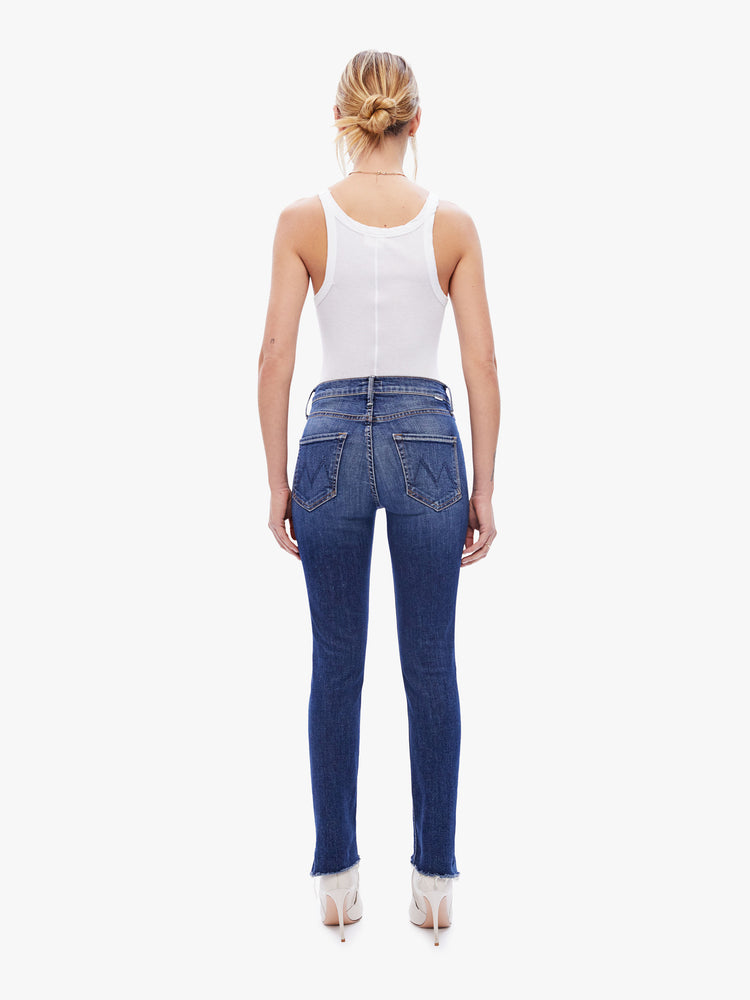 Back view of a womens dark blue wash jean featuring a mid rise, straight leg, and a step crop fray.