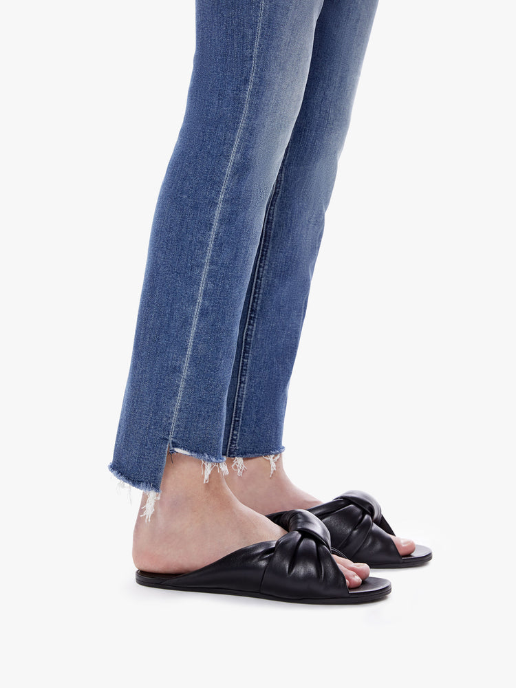 Side close up view of a womens medium blue wash jean featuring a mid rise, straight leg, and an ankle length crop step hem.