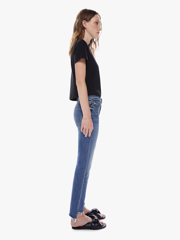 Side view of a womens medium blue wash jean featuring a mid rise, straight leg, and an ankle length crop step hem.