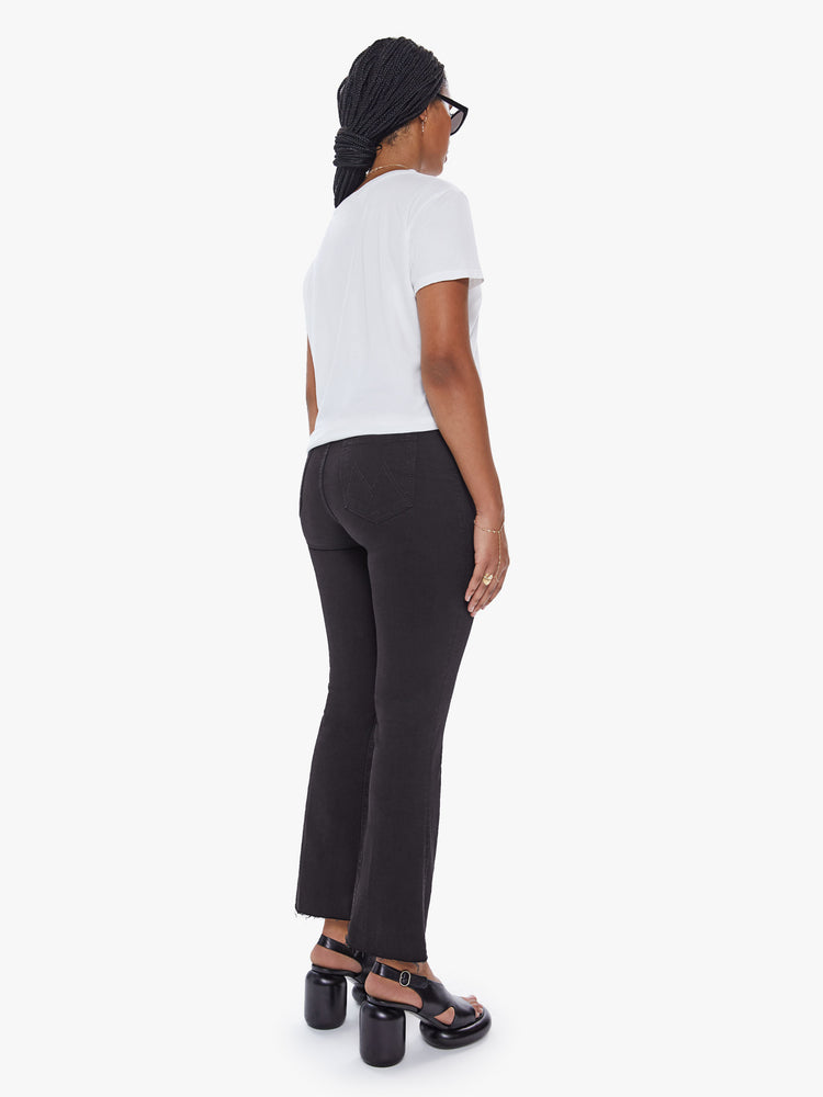 Back view of a womens black jean featuring a high rise, flare leg, and a raw cut ankle length hem.