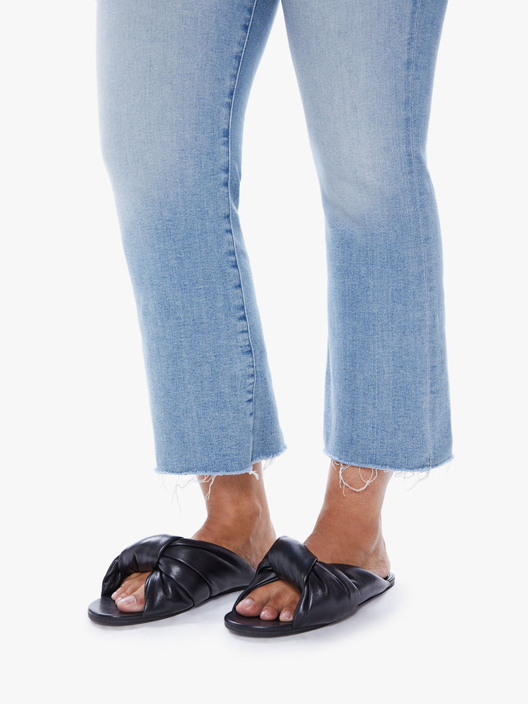 Side close up view of a womens flare pant leg in a light blue wash featuring a raw hem.
