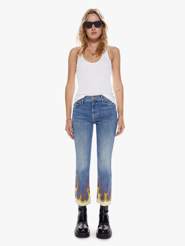 Front view of a womens boot cut hits at the ankle high rise medium blue wash jean with paint flames at the frayed hems