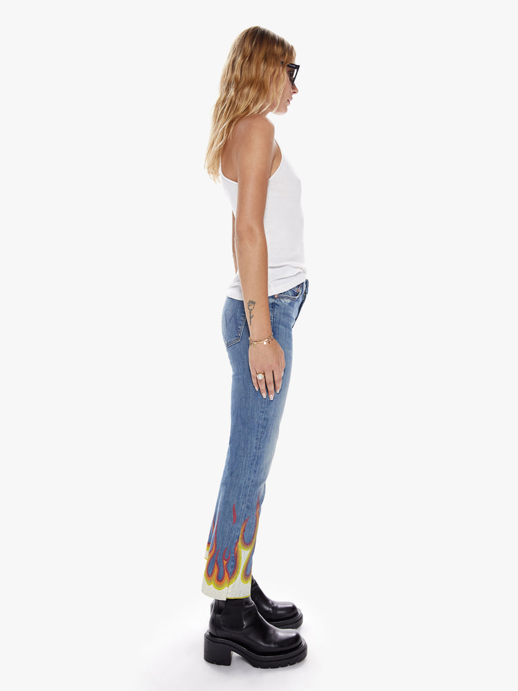 Side view of a womens boot cut hits at the ankle high rise medium blue wash jean with paint flames at the frayed hems
