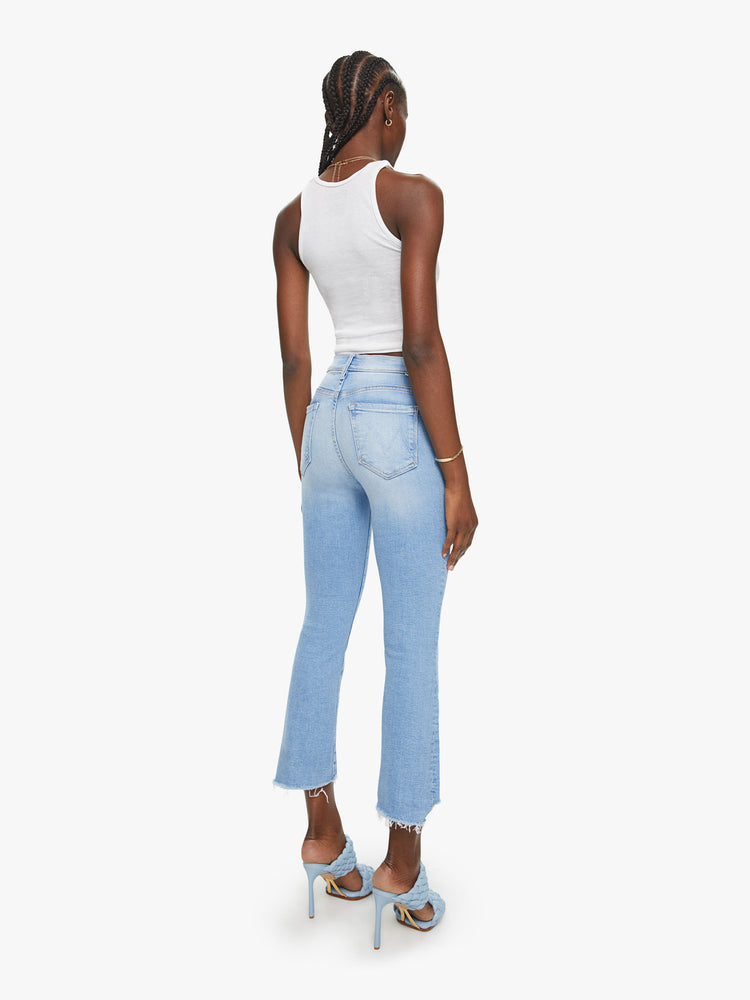 Back view of a womens light blue jean featuring a high rise, bootcut, and a crop step frayed hem.