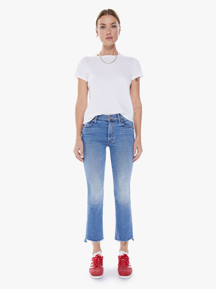 Front view of woman's high-waisted bootcut is cropped at the ankle with a frayed step-hem in a mid-blue wash.