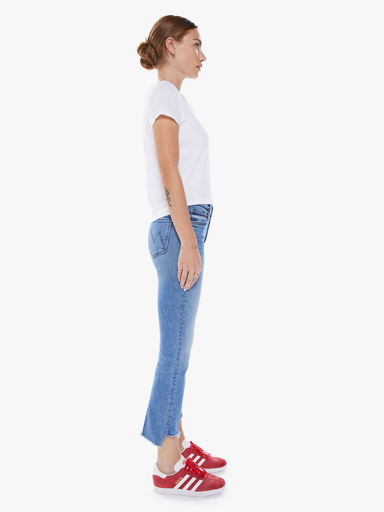 Side view of woman's high-waisted bootcut is cropped at the ankle with a frayed step-hem in a mid-blue wash.