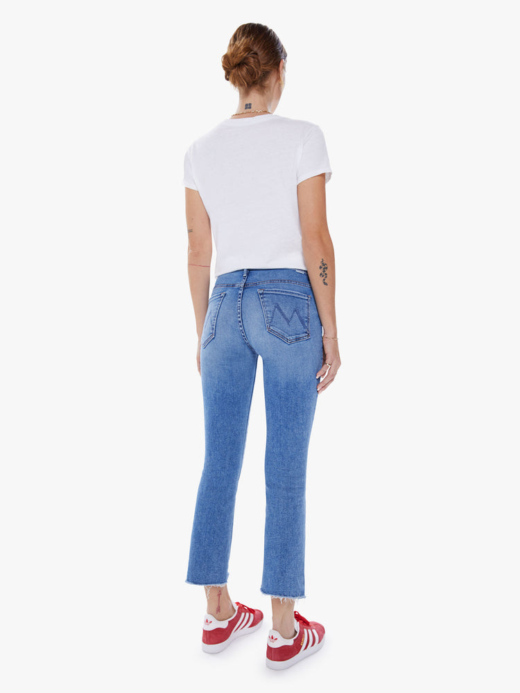 Back view of woman's high-waisted bootcut is cropped at the ankle with a frayed step-hem in a mid-blue wash.