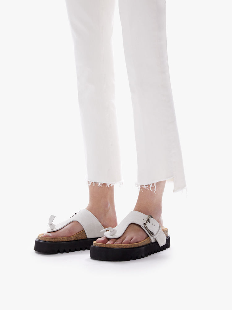 Hem close up view of a woman in a high waisted bootcut hits at the ankle with a frayed step-hem cut from comfortable stretch fabric in an off white hue with tonal hardware
