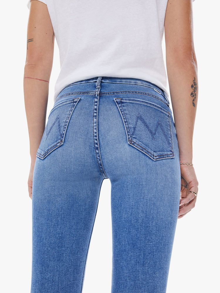 Back view of a woman's mid-rise skinny has an ankle-length inseam and a clean hem in mid blue wash.