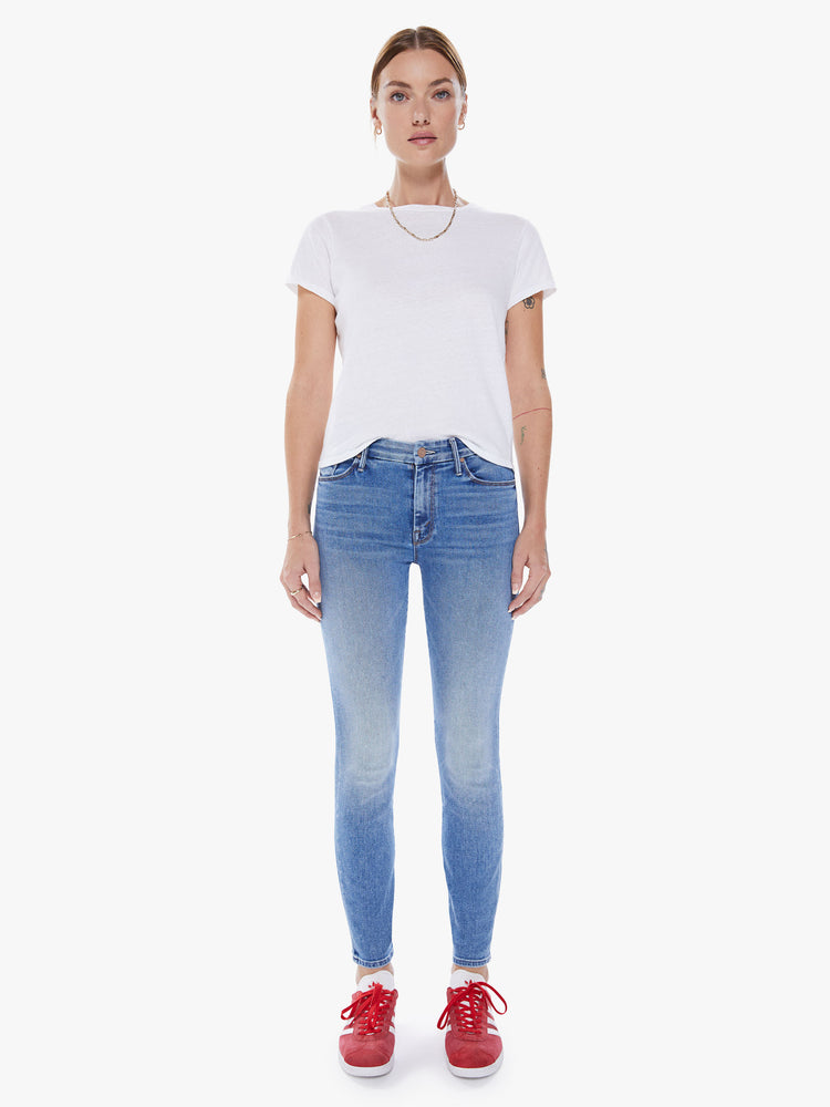 Front view of a woman's mid-rise skinny has an ankle-length inseam and a clean hem in mid blue wash.