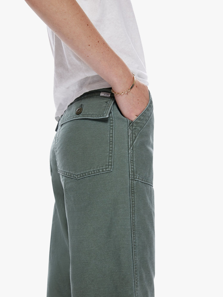 Close up back pocket view of a woman in a cargo pant featuring a high rise, wide leg, button fly and frayed ankle length hem, made from 100% deadstock fabric in a classic army green hue with tonal buttons