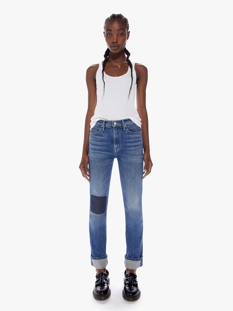 Front full body view of a woman in a mothers original straight leg jean with a mid ride and a cuffed ankle length inseam cut from a semi rigid superior denim in a mid blue wash with fading, whiskering and a patch just above the knee