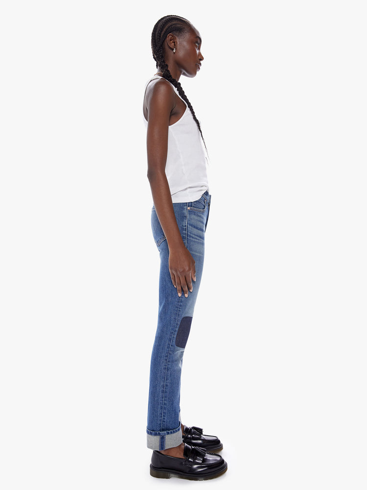 Side full body view of a woman in a mothers original straight leg jean with a mid ride and a cuffed ankle length inseam cut from a semi rigid superior denim in a mid blue wash with fading, whiskering and a patch just above the knee