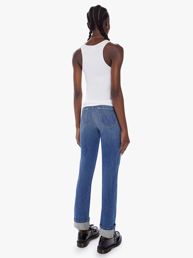 Back full body view of a woman in a mothers original straight leg jean with a mid ride and a cuffed ankle length inseam cut from a semi rigid superior denim in a mid blue wash with fading, whiskering and a patch just above the knee