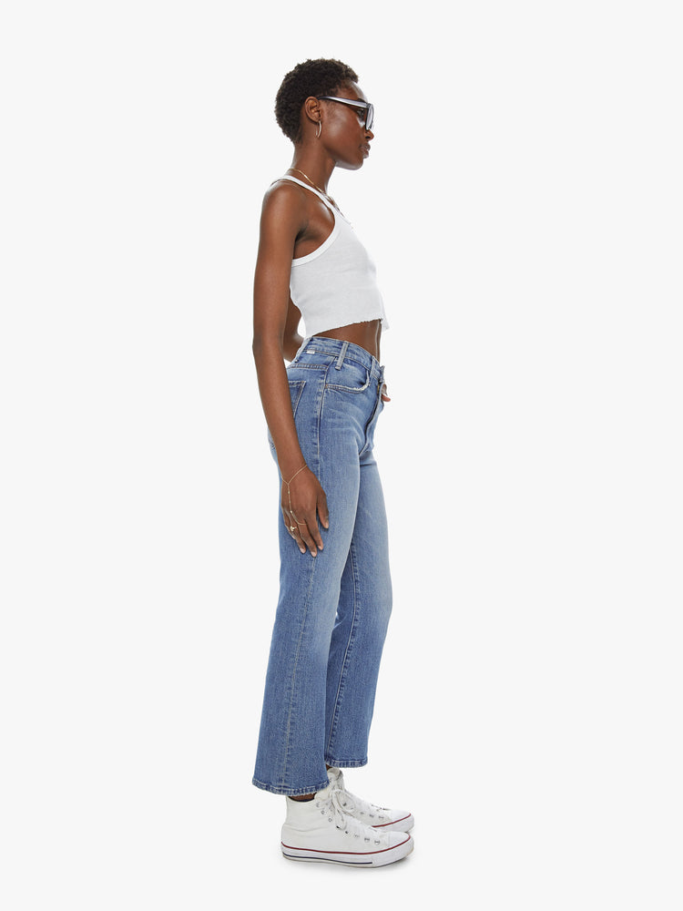 Side view of a womens high rise skinny medium blue wash jean with a flare leg, ankle clean hem and fading and distressed details.
