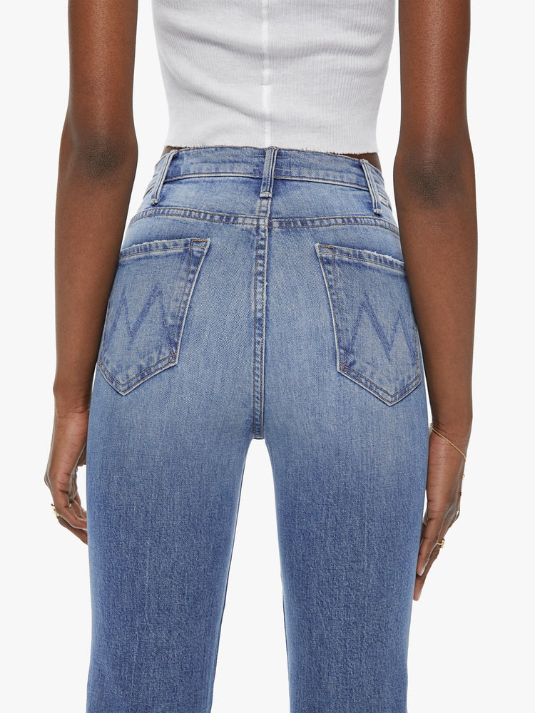 Back close up view of a womens high rise skinny medium blue wash jean with a flare leg, ankle clean hem and fading and distressed details.