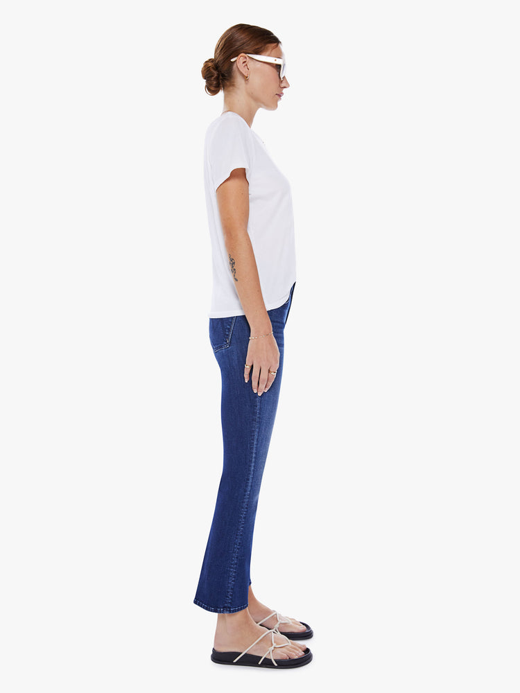 Side view of a woman mid-rise bootcut has an ankle-length inseam and a clean hem in a dark blue wash.