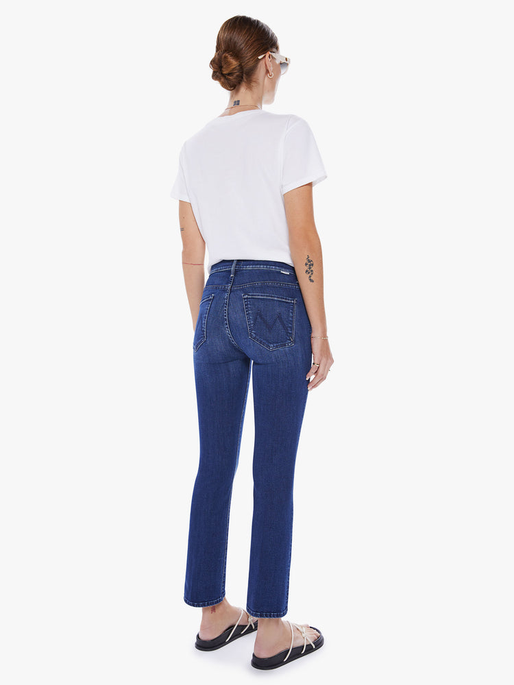 Back view of a woman mid-rise bootcut has an ankle-length inseam and a clean hem in a dark blue wash.