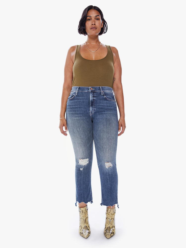 Front view of a womens high rise jean in a medium blue wash denim featuring an ankle length step fray hem and distressed knees.