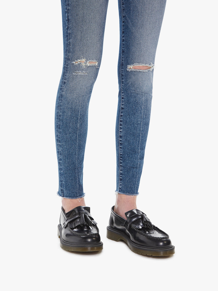 Hem detail view of a women's medium blue mid-rise skinny jean with distressing at the knees and a frayed ankle hem