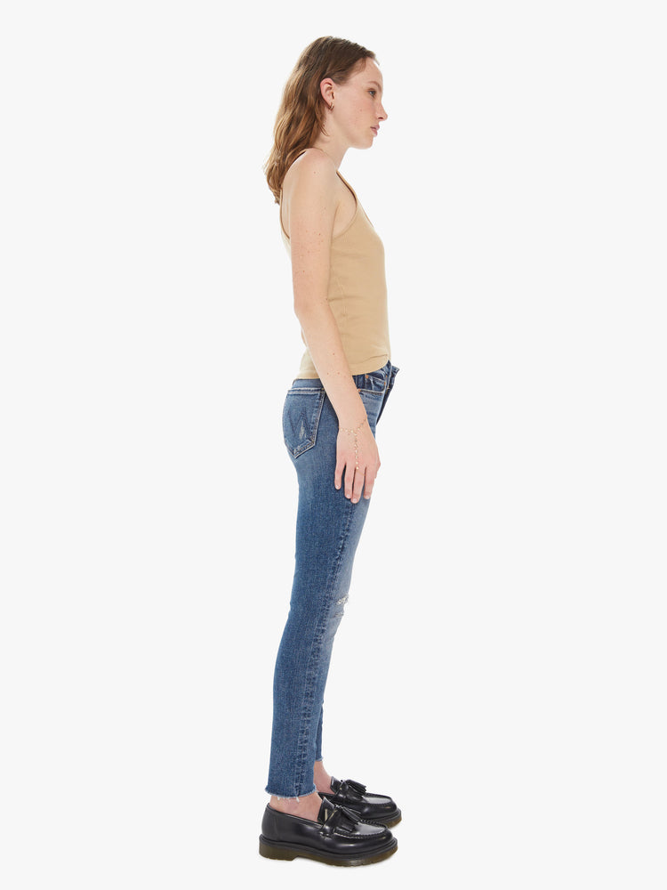 Side view of a women's medium blue mid-rise skinny jean with distressing at the knees and a frayed ankle hem