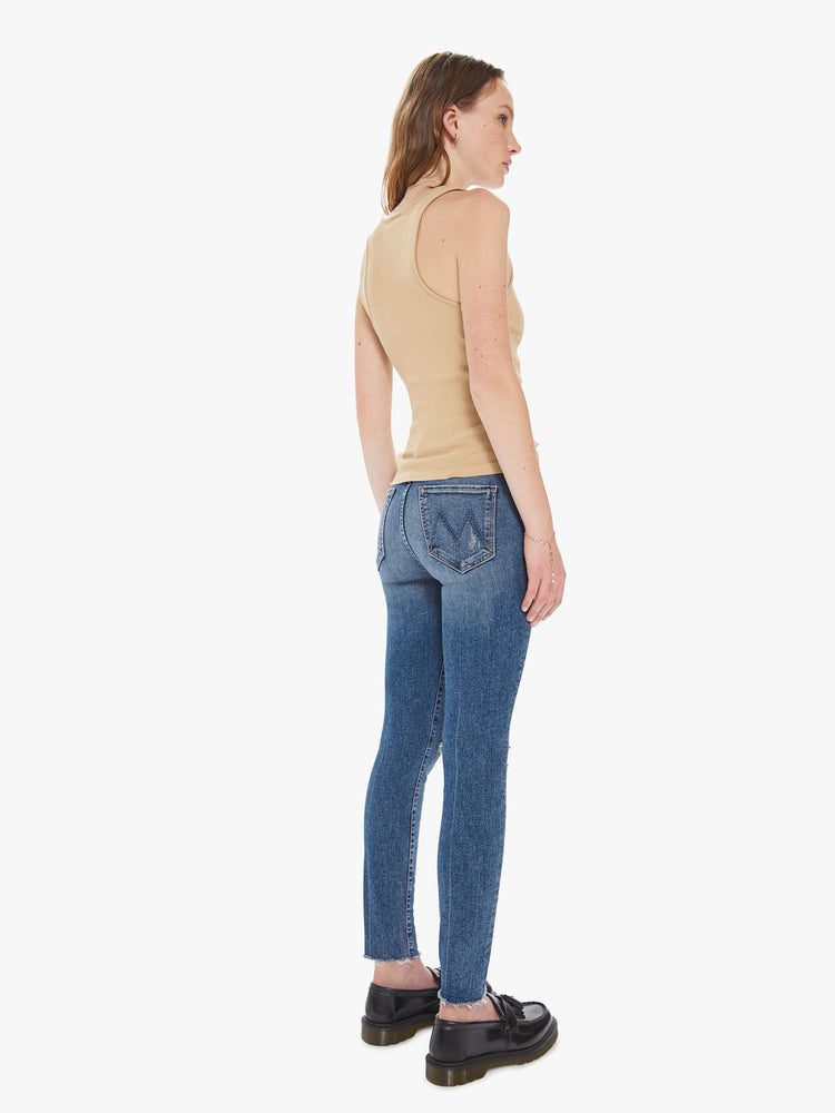 Back view of a women's medium blue mid-rise skinny jean with distressing at the knees and a frayed ankle hem