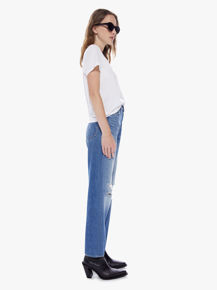 Side full body view of a woman in medium blue wash 90's inspired high rise straight leg and a clean hem with whiskering and tears at the knees