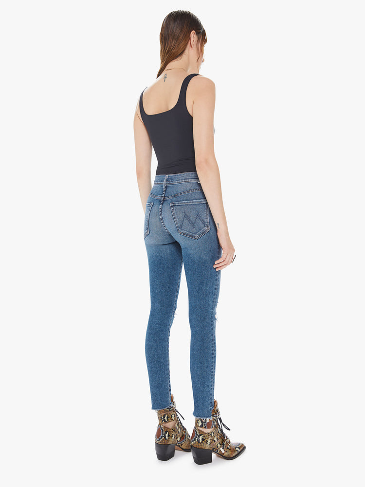 Back view of a womens medium blue wash jean featuring a super high rise, a skinny leg with a ankle length step crop fray.