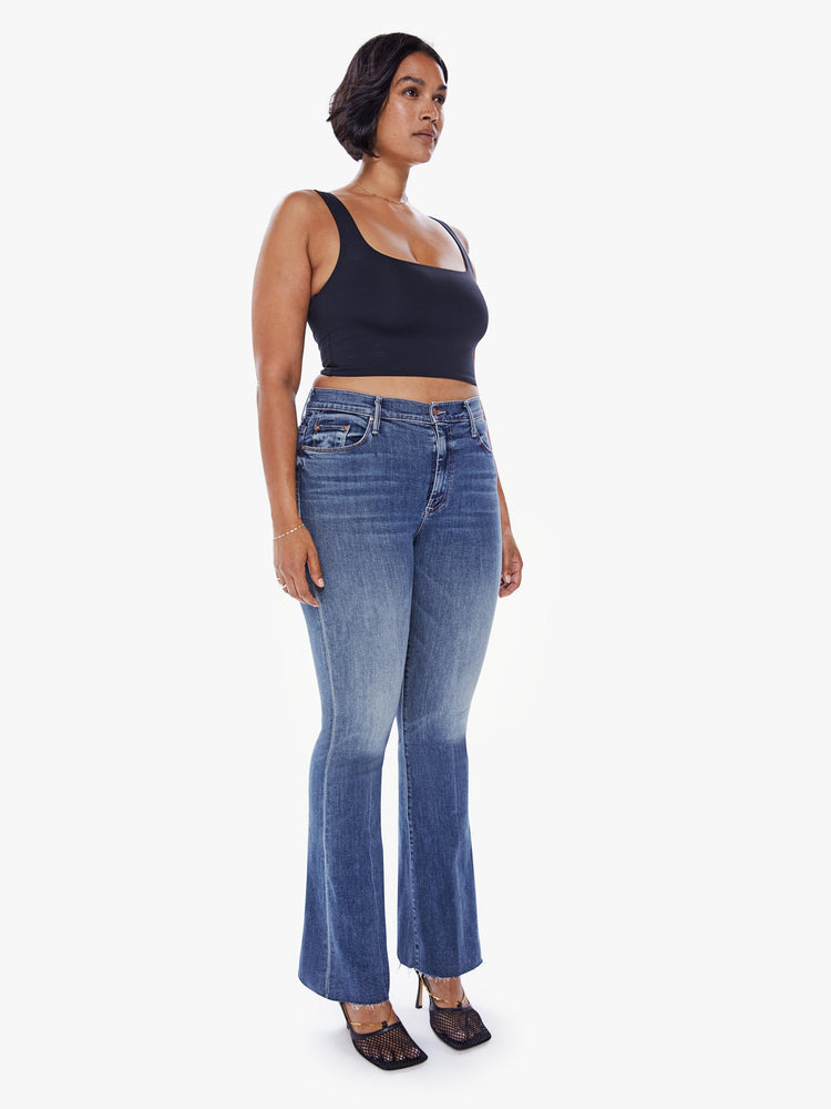 Front 3/4 view of a womens mid rise jean in a medium blue wash, featuring a flare leg with a raw hem.