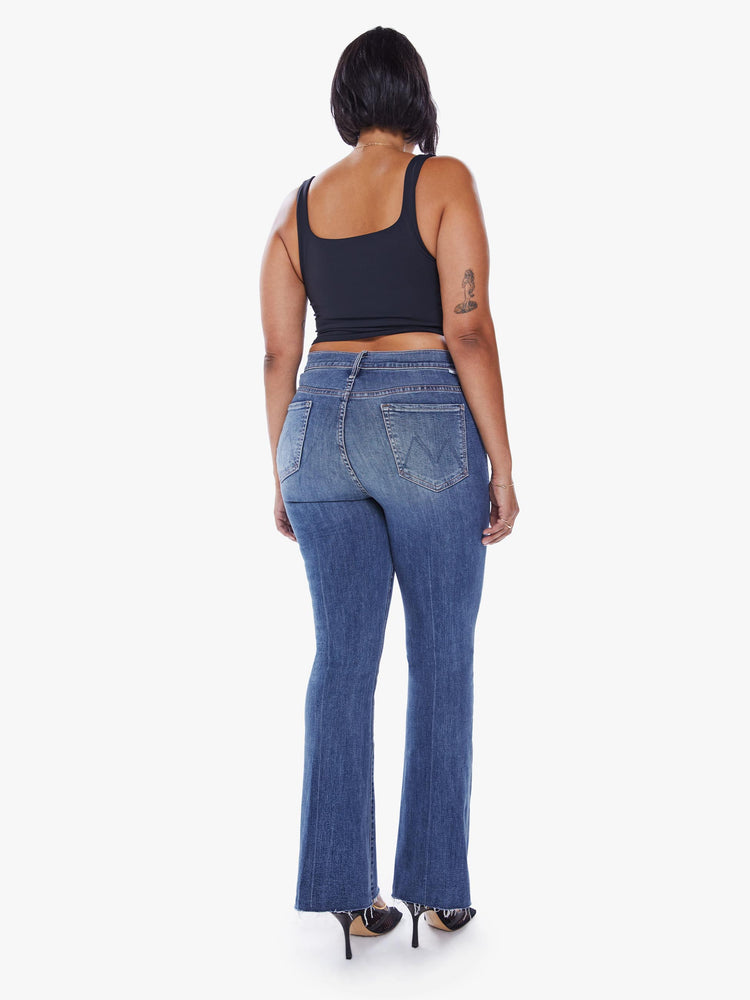 Back view of a womens mid rise jean in a medium blue wash, featuring a flare leg with a raw hem.