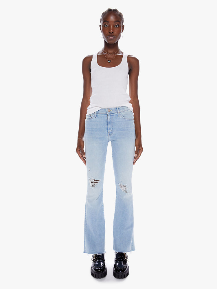 Front view of a woman in a cult-favorite flare jean with a midrise and a 31 inch length inseam and a frayed hem in a light blue wash with fading, whiskering, and tears at the knees, cut from denim with a touch of stretch