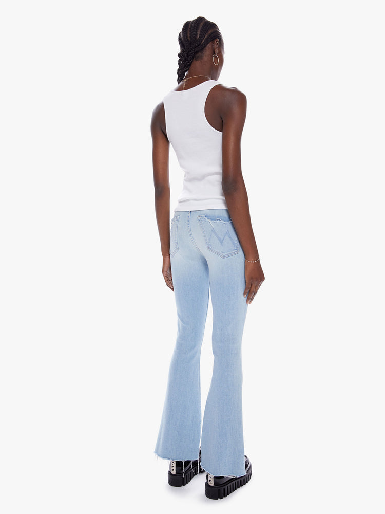 Back view of a woman in a cult-favorite flare jean with a midrise and a 31 inch length inseam and a frayed hem in a light blue wash with fading, whiskering, and tears at the knees, cut from denim with a touch of stretch