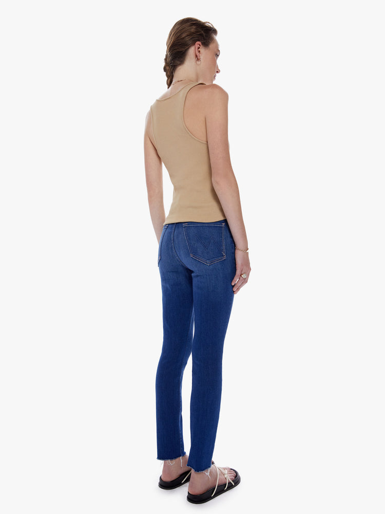 Back view of a woman high-rise skinny-straight leg with an ankle-length inseam and a frayed hem in a dark blue wash and fading at the knee.