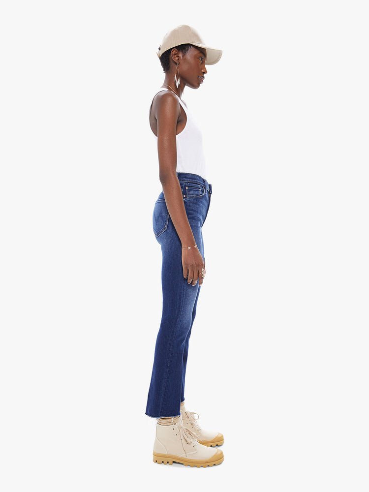 Side view of women's deep blue bootcut jean with fading and a frayed ankle length hem