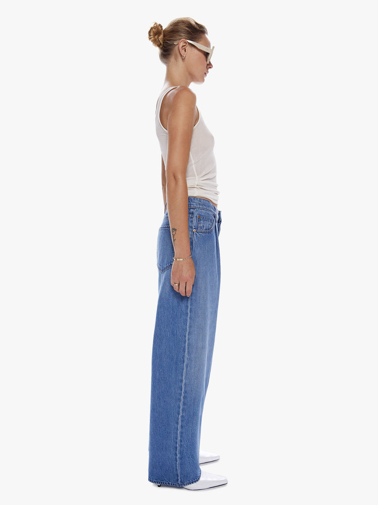 Side full body view of a woman in a wide leg jean from snacks from Mothers homeage to throwback styles of 80s and 90s designed to be worn loose and low at the hips, jeans feature a button fly, front pleat for an even roomier fit and clean ankle length inseam in a vintage blue wash