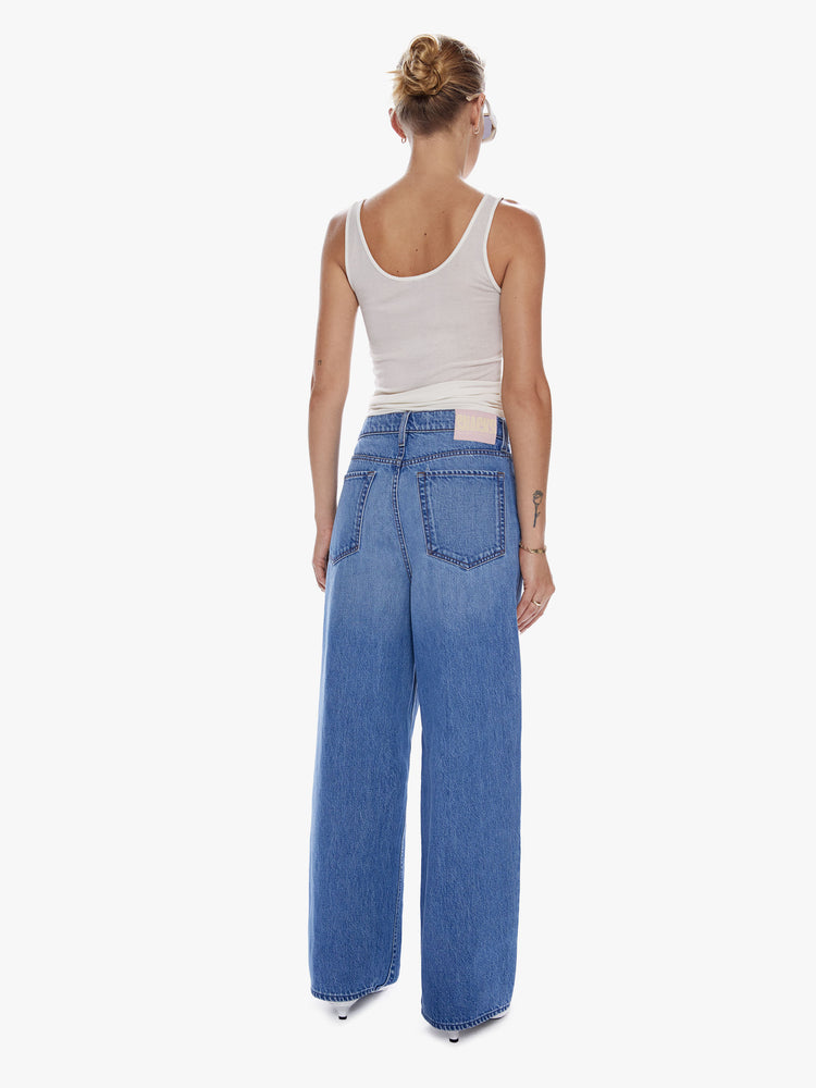 Back full body view of a woman in a wide leg jean from snacks from Mothers homeage to throwback styles of 80s and 90s designed to be worn loose and low at the hips, jeans feature a button fly, front pleat for an even roomier fit and clean ankle length inseam in a vintage blue wash