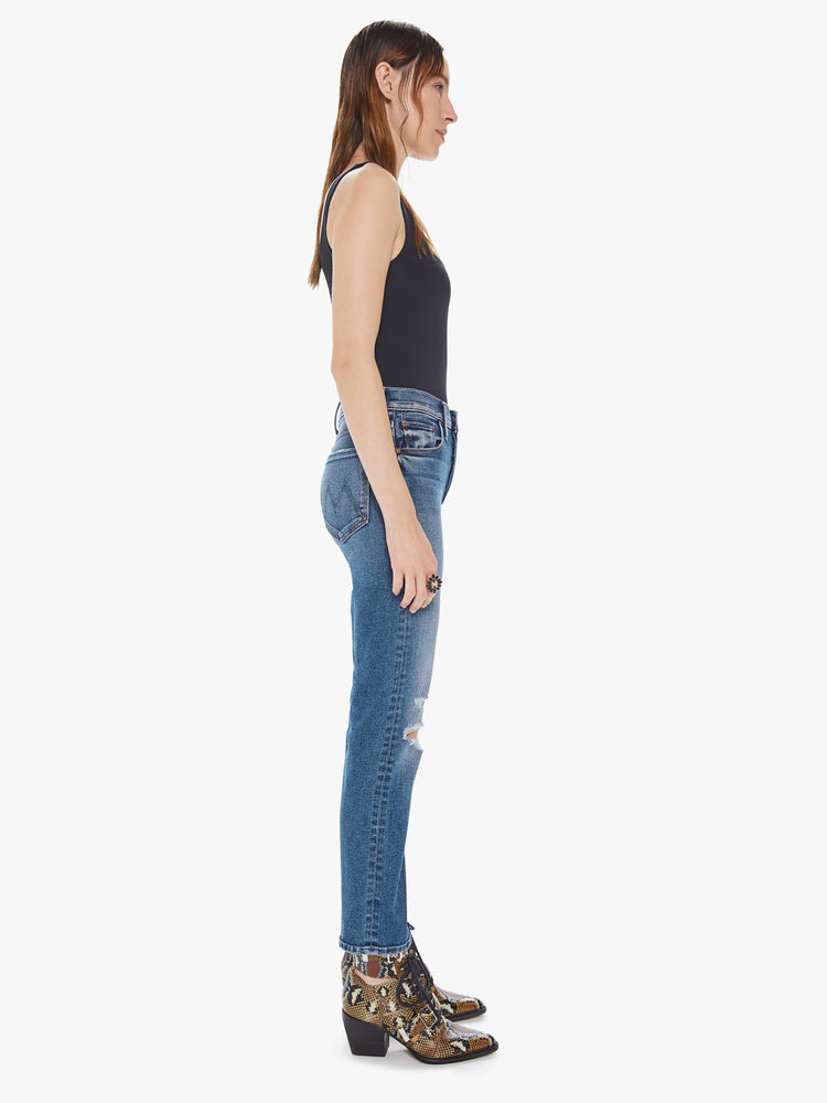Side view of a womens medium blue wash jean featuring a high rise, an ankle length straight leg, and distressed details at the knees.