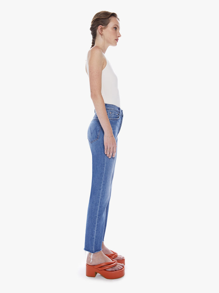 Side view of a woman High-rise jeans with a straight leg, button fly, ankle-length inseam and a frayed hem in a mid blue wash.