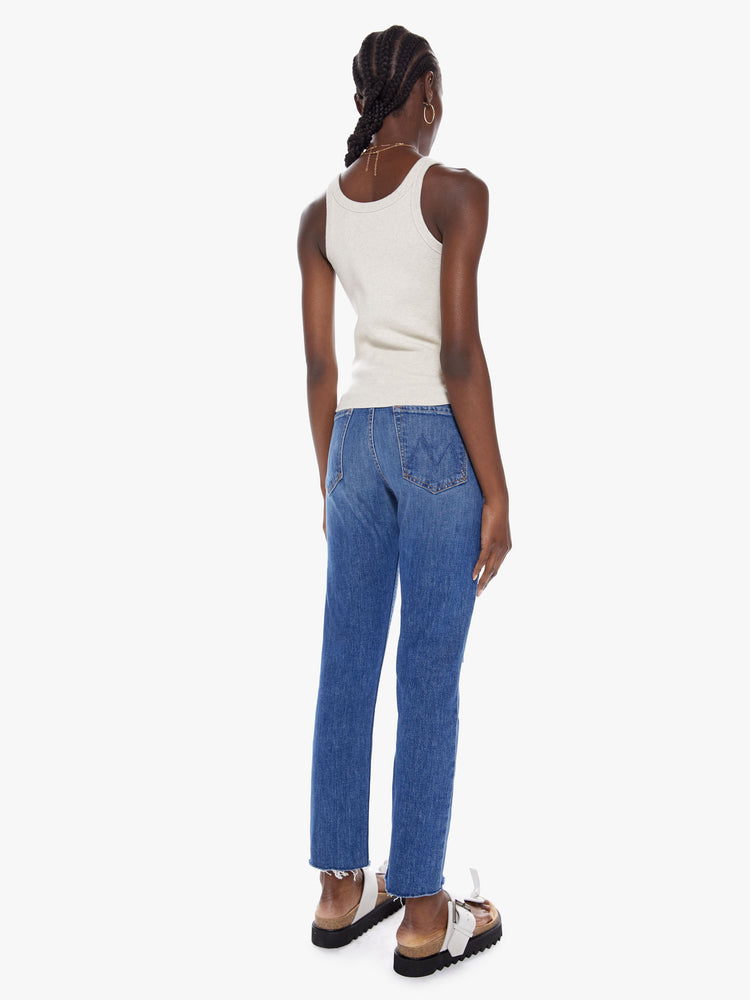Back full body view of a woman in a high rise jean with a straight leg, button fly, ankle length inseam and a frayed hem made with a touch of stretch in a mid blue wash with whiskering, fading and distressed details