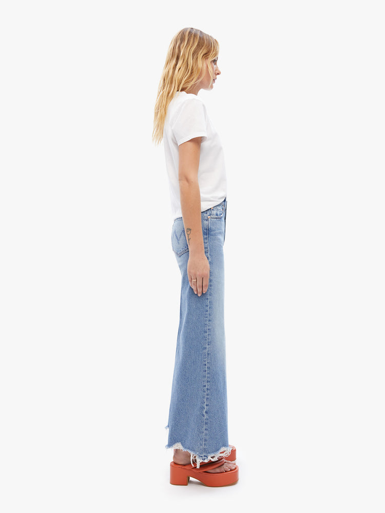 Side view of a womens high rise jean in a light blue wash featuring a wide, leg with chewed hem.
