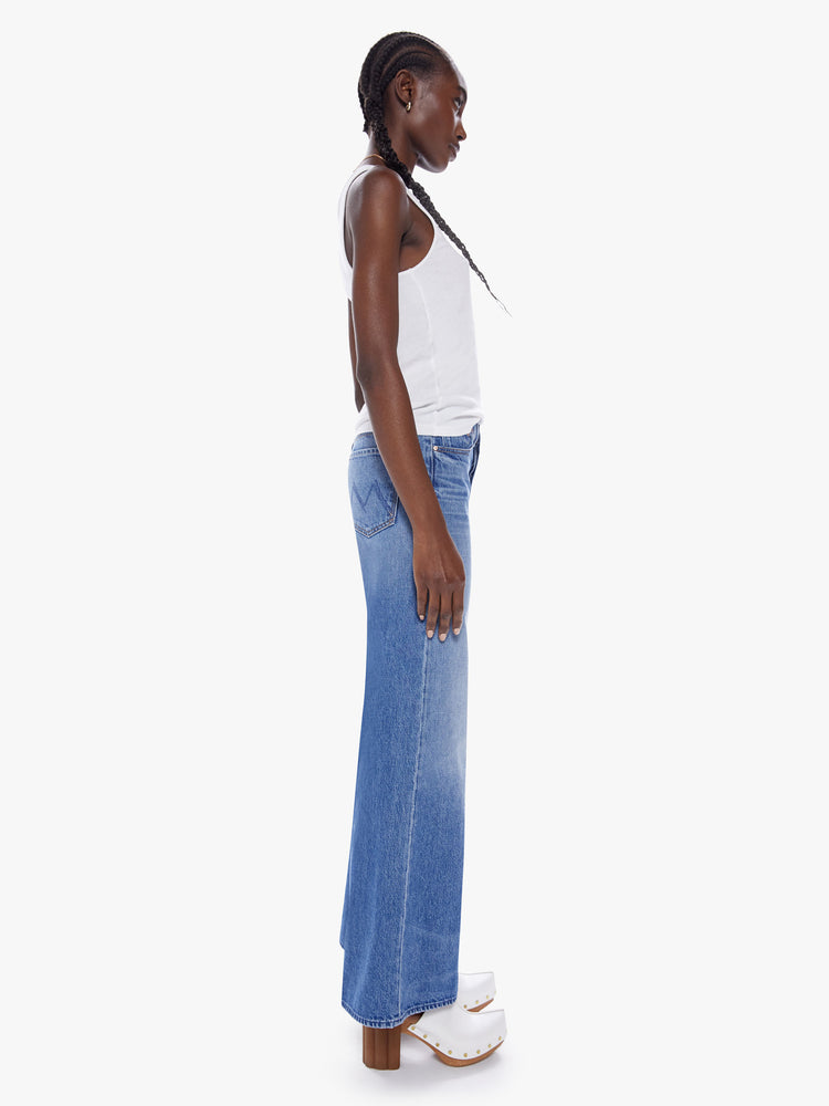 Side view of a woman high-waisted wide leg fit has a button fly, 31-inch inseam and clean hem in a mid blue wash cut from semi-rigid SUPERIOR denim.