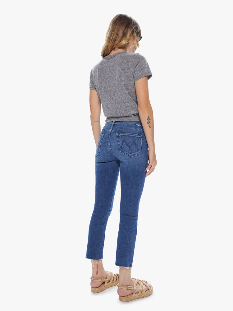Back view of a woman wearing medium blue wash jeans featuring a mid rise and a frayed cropped hem.