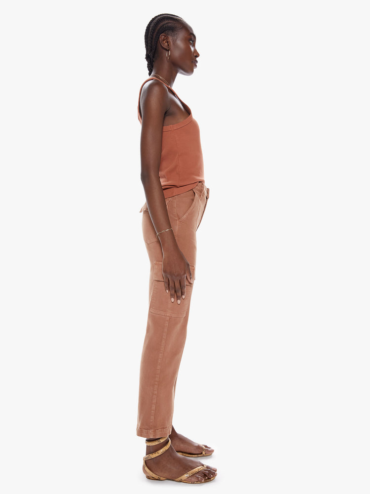 Side full body view of a woman in high waisted ankle length pants with a wide straight leg, button fly, cargo pockets and seams down the front made from a cotton blend with a touch of stretch in a faded rust hue with tonal hardware